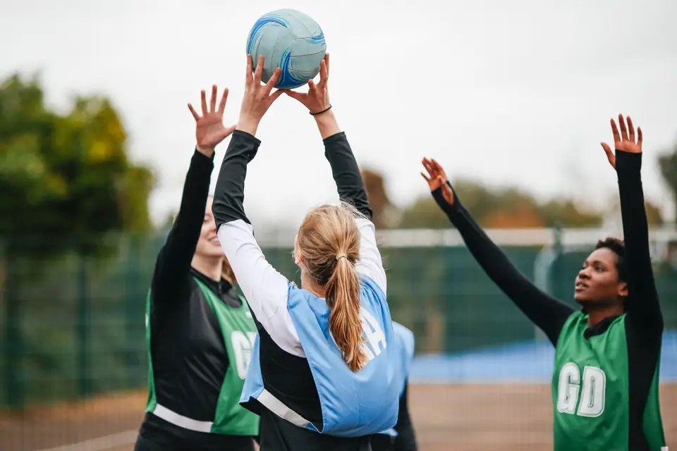 Netbalspelers reik na die bal tydens ’n buitelugoefening